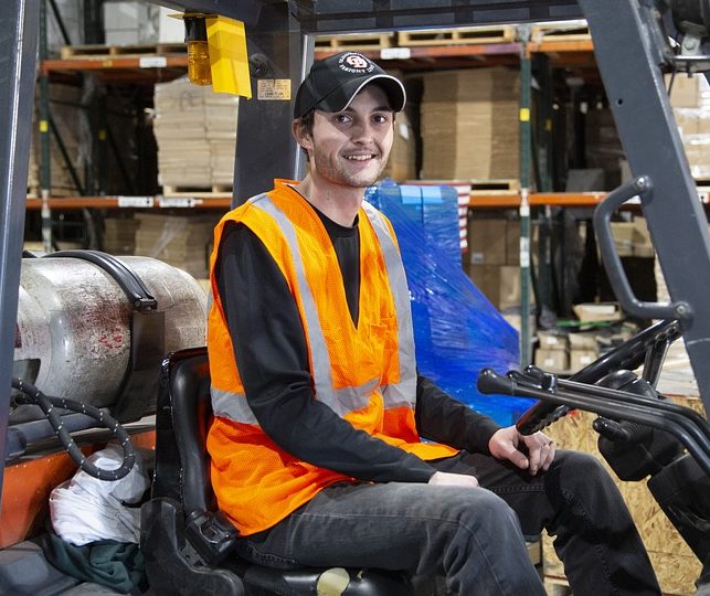 smiling male warehouse worker sitting on fork lift
